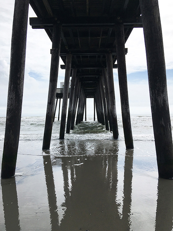 Water of ocean underneath a dock showing the reflection of the dock and skyline. At New Jersey.