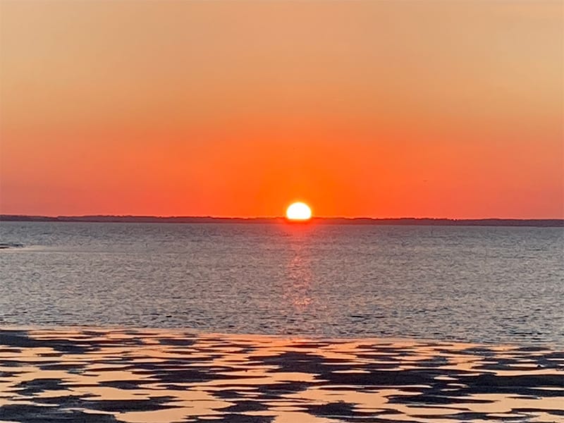A golden, orange, red warm sunset setting down into the horizon over the water. At Chincoteague Island, Virginia.