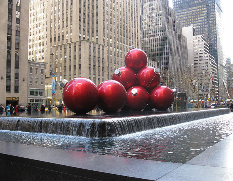 A display of gigantic Christmas red balls in the middle of the picture with skyscrapers in the background. Taken in New York City.